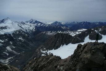 Belton regards the Cook District from the summit of Mount Darby, high out above the Mueller Glacier. If the view was magnificent, the consolation for not crossing into the Landsborough was non-existent. On the skyline from left to right: Sefton, La Perouse, The Footstool, Hicks, Dampier, Aoraki/Cook, the Minarets, Elie, Hochstetter Done, Darwin, Malte Brun, Mannering, and eventually The Nun’s Veil.