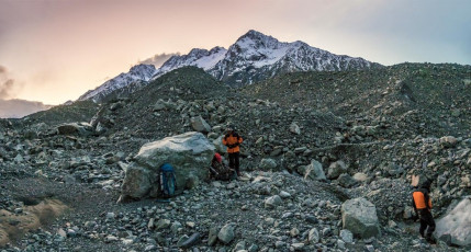 Back down on relatively flat ground again on the western edge of Tasman Glacier, time dragged as we shivered for another four hours until daybreak. As luck would have it, the weather began to improve rather than deteriorate as forecast. I was again amazed to see how, as soon as rain and snow ceased and sun shone, the moraine seemed to miraculously lock up. There was virtually no rock fall as we made our way along its base towards the terminal lake, searching for the best escape route. As we went tiny reservoirs of delicious water appeared in rock depressions – a few sips each time was better than nothing. We were surprised to see a helicopter flying up the centre of Tasman Glacier, thinking ‘that’s quick for the tourist operators to be up again after poor weather – another sign of the times’.
This image - At dawn, our second bivvy spot on the western side of Tasman Glacier.