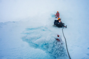 By now visibility was poor, so it took a while for it to dawn on me that the route we were following was unfamiliar to me and leading us into some much more exposed terrain than I’d expected. I found out later that we were on the summer route, which leads up into bluffs on the Shark’s Tooth side of the crater.
At 2,470 metres I reached a snowy shelf about a metre and half wide, with ice cliffs above and below. Then the snow squalls started. Ed and Will looked somewhat unenthused and I felt a heightened burden of responsibility. So I secured them both to the base of the final pole on the route, then went ahead up an exposed little section to see what lay ahead. Just over a rise I could see further shelving leading down on to the crater floor – we were near as damnit but, in the deteriorating conditions, we all agreed that going on was not a smart idea. In such poor viz it would also be rather pointless.