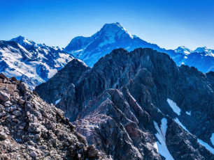At about 2,000m were stowed our crampons and climbed eastward back up onto the rocky ridge leading over Waihi pass (1,931m) to Kitchener (2,042m). If anything, the condition of the rock down here was at its worst, demanding constant concentration. Everywhere it was bone dry, fractured and tottering, making protection placement very difficult. At one point on a particularly treacherous section I took a short tumble while trying to dodge a rock Mike had accidentally dislodged above me. After that progress slowed further as we had to wait while one descended to a safe spot before the other followed.
We eventually reached the base of the summit cliffs of Kitchener and could see a steep chute that gave access to the summit. But a sheer section about ten metres high looked too daunting. We tried another line diagonally right but that only ended beneath sheer cliffs. “Hmmm, how can this be a one” we anguished. Surely it must be a winter grade, when there’s a lot more snow about to work with and things are frozen together. Time for lunch and a rethink.
From our sandwich point we just couldn’t see a safe way up. Reluctantly we concluded that the sensible thing to do was to retreat and traverse around on the west side to reach Mueller Hut. We also noted that the top didn’t look particularly friendly either. What if we did manage to climb to the top and there was no way forward? We certainly wouldn’t want to down climb the way we came up without bullet proof protection. So, down we went.