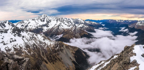 As I reached the end of the traverse and gained the ridge at 2,070m, I noticed how fog had filled the Travers Valley and the sky above had filled with brooding, spectacularly beautiful clouds. It was very nice to relax for a bit on safe ground as I watched Simon, then Caro make their way across the traverse. When they both joined me we commiserated about how the sustained, un-protectable exposure had incidiously broken our resolve. It was as though our anxiety had slowly snowballed to the point where our thoughts were no longer about the summit. As we took in the deteriorating weather, which appeared to be bearing out the unfavourable forecast, we made the call that it was time to find a way down that didn’t involve down climbing what we’d just come up.