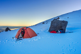 Sealed in my bivy bag, fully clothed except for my boots, with delicate pieces of my condensed and then frozen breath dropping on my face, I felt no fear. So my rapid breathing was a physical rather than emotionally driven response to my situation. But having endured it for three hours, the knowledge that I had another nine to go until dawn didn’t fill me with joy.
My two young Spanish companions, Juan and Raoul, lay shivering a few metres away in my slightly less frigid two man tent. Raoul had been a last minute addition to our party, so perhaps Juan felt a twinge of guilt that I was outside. He offered me his little travel pillow, which I gratefully accepted. In so doing I exposed my face and almost immediately my breathing settled down. Ah ha, maybe I’m susceptible to mild claustrophobia. That could explain my dislike of crowds and shopping malls. This image - Our camp (1,820m) between Tongariro and the North Crater rim, waiting for the sun to warm things up.