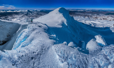 While we waited I suggested we climb up onto the top of Tukino, just twelve metres lower than neighbouring Te HeuHeu. This was my third time up Te HeuHeu and, until then, I’d never bothered to visit Tukino’s summit. I’m glad we did, because it’s a spectacular spot – a narrow outcrop of rime ice with sheer drops on three sides.
The others still hadn’t appeared on top of Te HeuHeu, but we reasoned that they were three and well experienced. They must be fine, so began our descent down the west ridge to Ruapehu’s Summit Plateau. As we trudged towards the top of Mangatoetoenui Glacier three waving figures appeared above the ice cliffs. It was good to know for certain they were also on their way down.
This image - Looking to Te HeuHeu (2,732m) from the exposed summit of Tukino (2,720m).