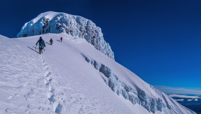 Simon belayed Felix up first and then decided he’d had enough of standing in the persistent, icy wind. “Dad says all three get on the rope” yelled messenger Felix through the spindrift. Hmmm, well, okay then. Soon Caro, then Kathy and I, bringing up the rear, climbed up the steep chute of rime ice. The very start of the chute was the crux, where having a top rope paid dividends.
By late morning we gathered at the base of the final ice cliff and agreed that Kathy and I would bypass the cliff, traversing right, underneath until it relented and became the west ridge. The others would do battle with the rime ice. This image - Approaching the second larger ice pitch at about 2,670m on the SE Ridge.