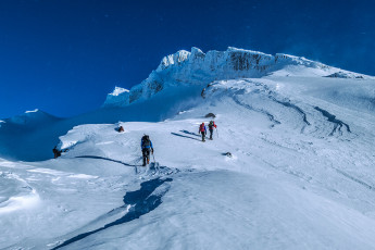 From the ski field we traversed across to the lower southeast ridge and began gaining height in earnest. Conditions were really good, but our first little challenge presented at 2,400m, where the icy wind had scoured away the snow, leaving a hard steep section of ice with a yawning drop below. Simon, Caro and Felix forged ahead while Kathy and I enjoyed our first pitch of the morning. That followed shortly after by our second, which was on the line of ice cliff that stretches horizontally right, appearing to be about three quarters of the way up the route, when viewed from TASC Lodge. This image - Ascending the SE Ridge of Te HeuHeu, here at about 2,300m.