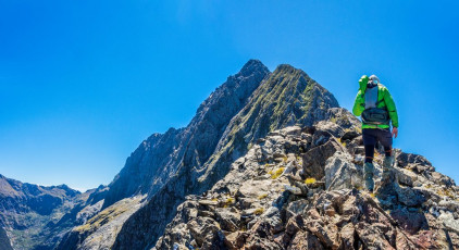 “I think we’re going to run out of time guys” I said. “Maybe, let’s discuss it and make a call” replied Caro. Simon stepped down off the next little vertical stairway and asked “What’s our height?” “1,430m with 250 still to climb” I replied. “It’s taken us about two and half hours to get here. Maybe another hour to the summit. Down climbing won’t be much quicker than going up with this level of exposure. Say mid-day by the time we reach camp. We know we’ve got a four hour descent from there and we’ll be tired and dehydrated. Making the 5pm pickup is doable but leaving no margin for error.” We all agreed. The view from where we sat was sufficiently awesome, we already had the satisfaction of climbing the crux and our fifty plus year-old bodies wouldn’t appreciate conforming to such a tight deadline. Added to this, the forecast was for a change to rain and we could already see cloud building around us. The thought of descending the steep, dense Fiordland bush beyond the treeline in the wet made me grimace. Down we went. This image -  Near the notch at the far end of the horizontal section, about 1,250m.