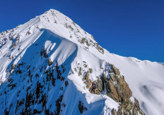 Our first little serving of gnarl came in a notch at 1,800 metres. A load of steps dropped left (south) off the ridge to avoid a steep narrow buttress. One set of steps carried on up along the edge of the buttress. “What do you reckon Pete – up or down?” “In these conditions up I reckon James. Is it ok on the far side of this thing?” James had climbed Rome Ridge as far as Low Peak the previous year. “Yeah, no problem from memory. Want to rope up or anything?” “Nah, I think it looks okay.” I led up. In hindsight James’ suggestion to rope up was the right one. There was just a small vertical rocky section where the snow and ice were thin that justified it, but those few steps were very exposed. I tentatively climbed up okay but, in so doing, disturbed the already tenuous snow. And the rope was in James’ pack. “Err… Hmmm … my axe just went right through there… Hmmm…” I held my breath while James picked his way up to join me. 
This image - This little step required care as the snow and ice were thin and unstable (Photo by James Hobson).