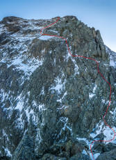 At the notch at 2,000 metres we gazed down to the narrow snow splattered saddle, then up the mostly snow-free but verglas-coated face giving access to the summit slabs. Ice filled sections of the crack that the first pitch follows. The early morning sun glistened on ice-covered mossy slabs above. Cough or no cough, it looked too dangerous to me. James is a far better rock climber than me and felt that he could still make progress on the crux pitches. His main concern was the exposed slabs above. We agreed that, if they were more of what we’d encountered on our way to the notch, then it was time to back off.