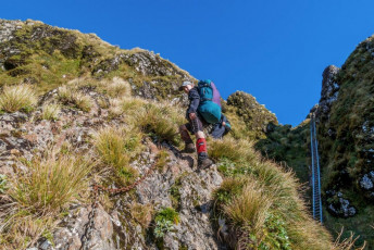 After a flurry of photos, I joined Ed and Will beneath the ladder. “So the hut’s not far now eh?” asked Ed. “Must be close” was my reply. I went on ahead so I could photograph them coming towards me around the dramatic, chain-protected section skirting underneath the summit of Tunui, before rejoining the main ridge. Back on the ridge, I copped some flak from the teenagers when they discovered how far away Maungahuka still was. My clouded memory of my first visit clearly needed some updating.  This image - On the chain protected route beneath the ladder, which goes beneath Tunui before rejoining the ridge west of Maungahuka Peak (1,330m)