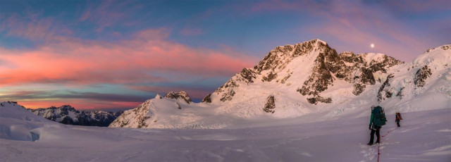 That evening back at a deserted Plateau Hut the radio sched revealed no new weather news, so our thoughts turned to our walk out next day, before the weather was forecast to get ugly on Friday. Given the snow condition, our main concerns about our descent route focused on crevassed terrain across the Plateau, and particularly the steeper southern side of Cinerama Col. We figured that if we could get over that and down the Boys Glacier before nightfall, then we should be fine. First red flag! 
Thursday dawned with a soft breeze and the first signs of weather-changing cloud. We set off in glacier travel mode right on dawn, so that picking a route through the crevasses would be easier. It was another great day to be in the mountains, especially the biggest ones in New Zealand.
This image - Crossing the Grand Plateau. As the sun rose the moon set behind Dampier.