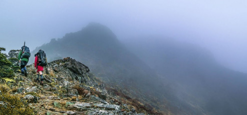 During the night rain fell, accentuating the cosiness of my sleeping bag. Next morning, the mist and drizzle outside encouraged us to get away in a leisurely manner. Depending on how the weather panned out, we would try to reach Old Man Hut, which involves a nice stretch of tops travel. But if the weather remained poor there was no point in covering that ground in clag, so we had the option to call a short day by staying at Slaty Hut, which is what happened.   
This image - Heading southeast along the ridge, at about 1,250m, between Mt Starveall and Mt Slaty.